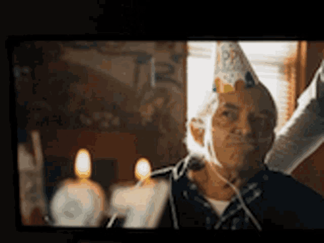 an elderly man wearing a birthday hat is sitting in front of a birthday cake