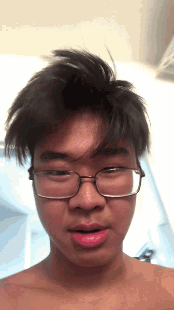 a shirtless young man wearing glasses looks at the camera with his mouth open