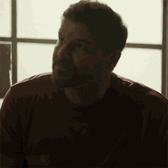 a man with a tattoo on his face is wearing a red t-shirt