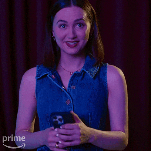 a woman in a blue denim vest is holding a cell phone in front of a prime logo