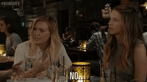 two women sitting at a table with a candle that says no on it