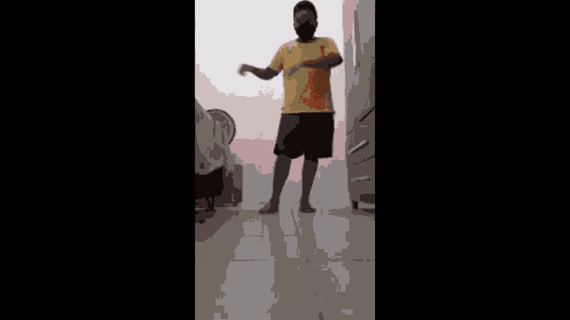 a man wearing a yellow shirt and a black mask is squatting down .