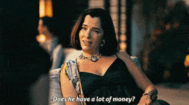 a woman is sitting on a couch talking to a man and asking him if he has a lot of money .