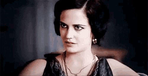 a close up of a woman wearing a necklace and earrings looking at the camera .