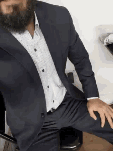 a man with a beard wearing a suit and white shirt is laying on a bed .