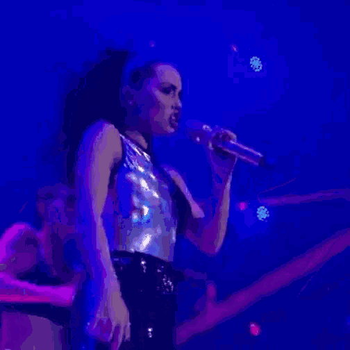 a woman is singing into a microphone on a stage in a dark room .