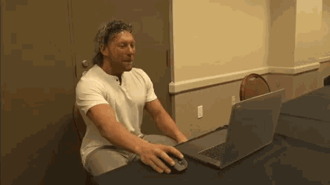 a man in a white shirt is sitting at a table using a laptop