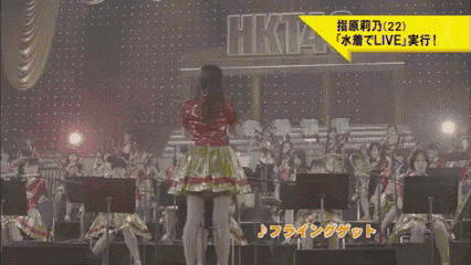a woman stands on a stage in front of an orchestra and a sign that says hkt48 on it