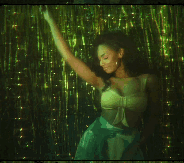 a woman in a yellow bra is dancing in front of green tinsel