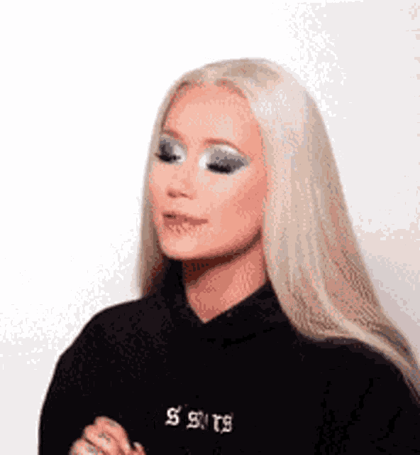a woman with blonde hair and blue eyeshadow is wearing a black hoodie and making a funny face .