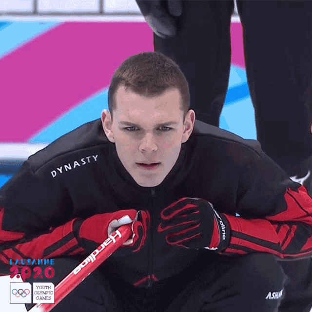 a young man in a dynasty jacket holds a red curling stick