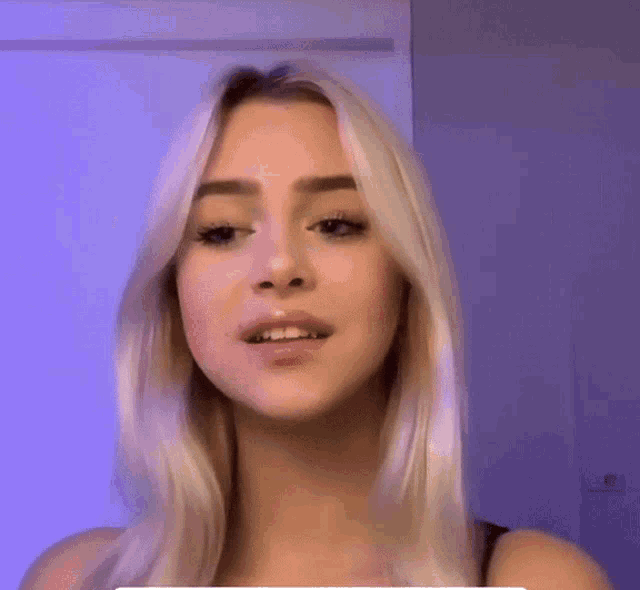a woman with blonde hair is making a funny face in front of a blue wall .