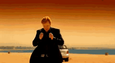 a man in a black suit is standing in front of a car on a beach .