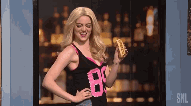 a woman in a tank top with the number 80 on it is holding a hot dog and smiling .