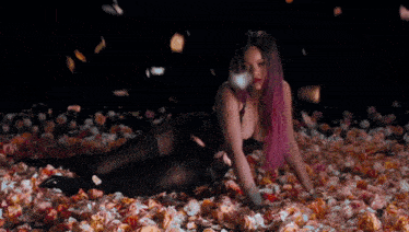 a woman with pink hair is laying in a pile of flowers