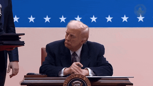 a man in a suit sits at a desk with the president of the united states seal on it