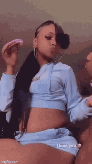 a woman in a blue crop top and shorts is holding a pink donut and saying i love you .