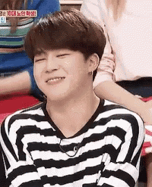 a young man wearing a black and white striped shirt is smiling while sitting in a chair .