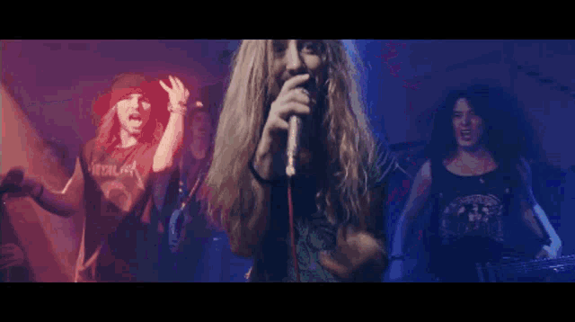 a man with long hair singing into a microphone in front of a group of people