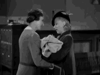 a black and white photo of two women holding a baby in a room .