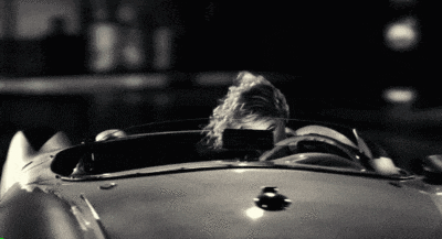 a black and white photo of a man driving a sports car