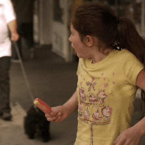 a girl wearing a yellow shirt with cupcakes on it is holding a popsicle
