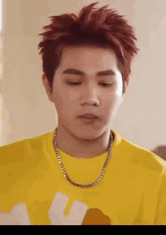 a young man with red hair is wearing a yellow t-shirt and a chain around his neck .
