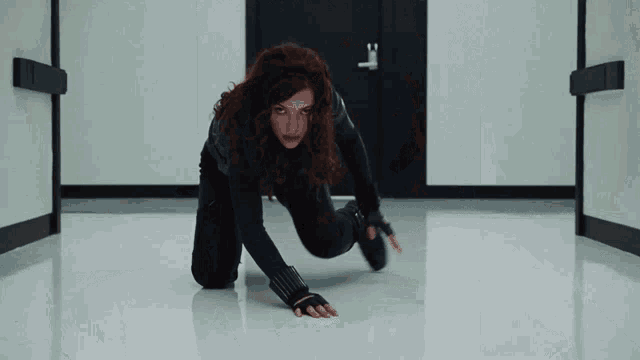 a woman in a black suit is crawling on the floor in front of a door with the letter t on it