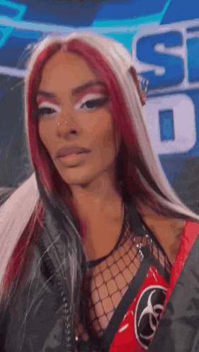 a woman with long red hair and white eyeshadow is wearing a black jacket and a red shirt .