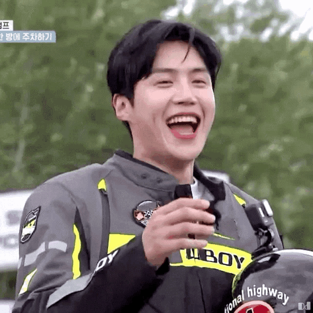 a young man in a motorcycle jacket is laughing while holding a bottle of beer .