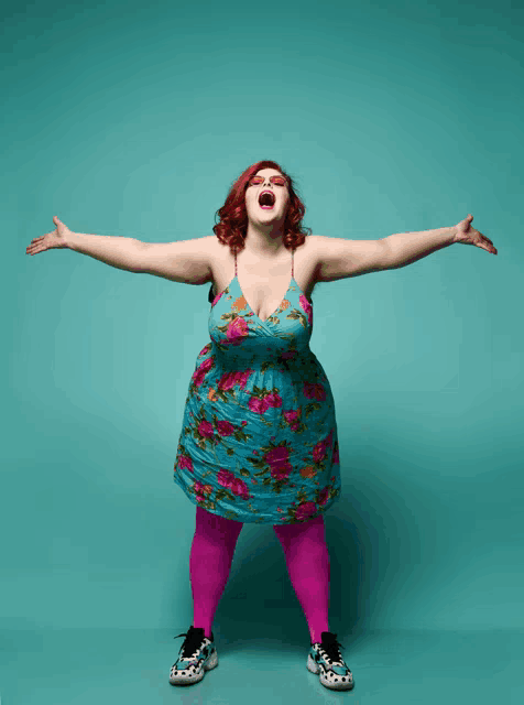 a woman in a blue floral dress and pink tights is standing with her arms outstretched