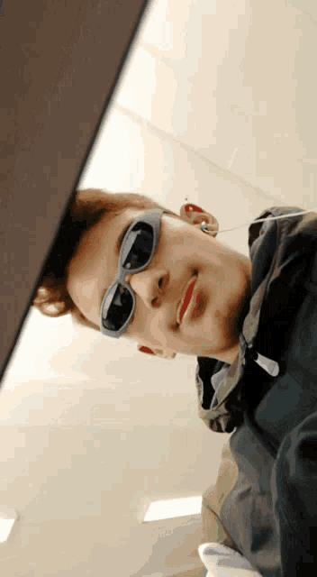 a young man wearing sunglasses and ear buds looks down at the camera