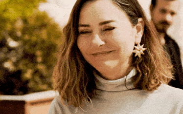 a woman wearing a turtleneck and earrings with a star on them is smiling .