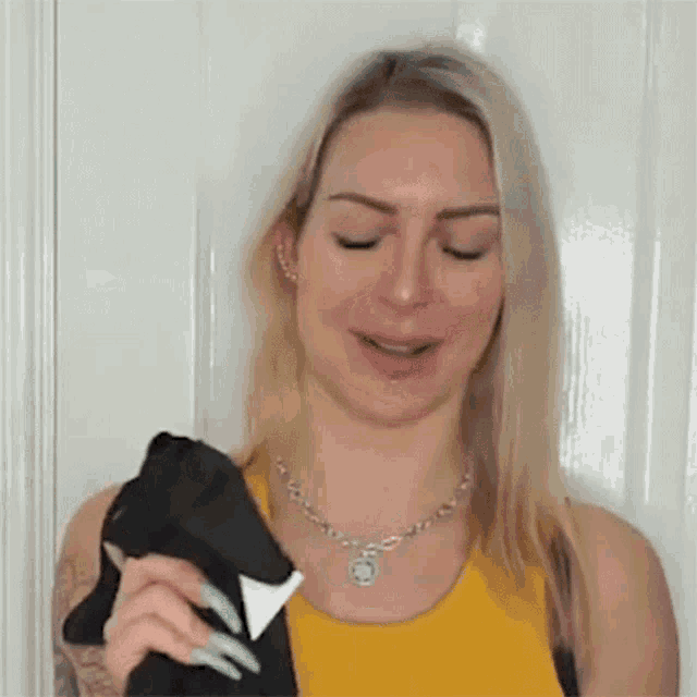 the woman is wearing a yellow tank top and a necklace and is holding a pair of socks .