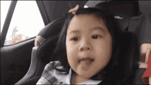 a little girl is sticking out her tongue while sitting in a car seat