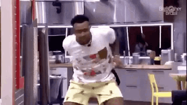a man is dancing in a kitchen wearing yellow shorts .