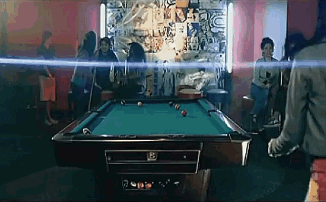 a pool table in a room with people sitting around it