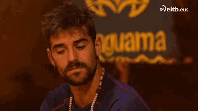 a man with a beard is sitting in front of a sign that says guaima