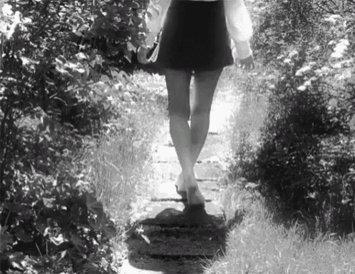a black and white photo of a woman walking on a path .