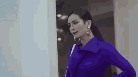 a woman in a blue coat and hoop earrings is standing in front of a door .