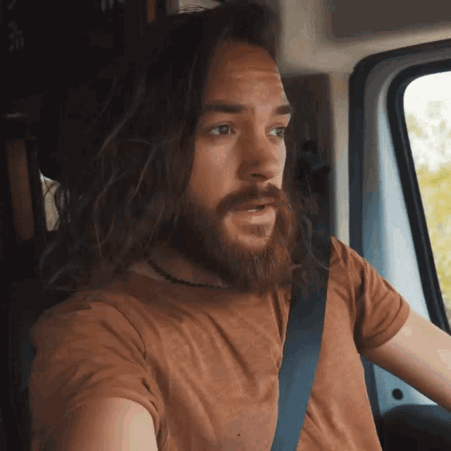 a man with long hair and a beard wearing a brown shirt