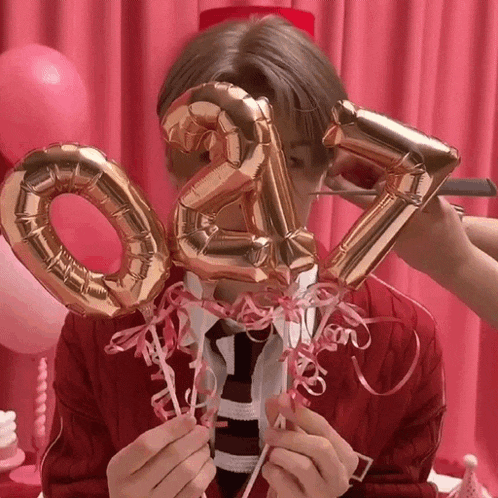 a man in a red sweater and tie is holding up balloons in the shape of numbers