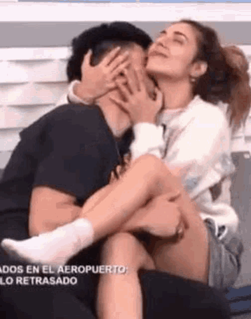 a woman is kissing a man on the cheek while he covers his face with his hands .