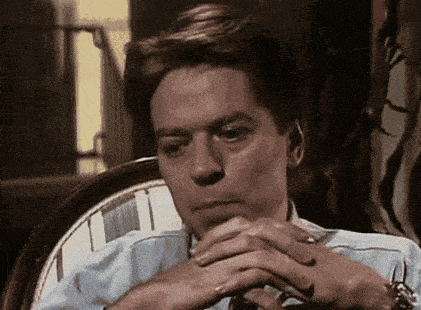 a man is sitting in a chair with his hands folded on his chin