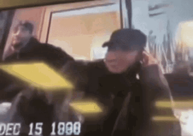 a man in a baseball cap is talking on a cell phone while standing in front of a window .