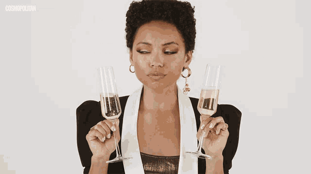a woman is holding two glasses of champagne in front of a cosmopolitan.com logo