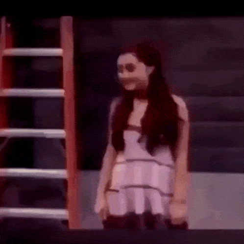 a woman in a white dress is standing in front of a ladder in a dark room .