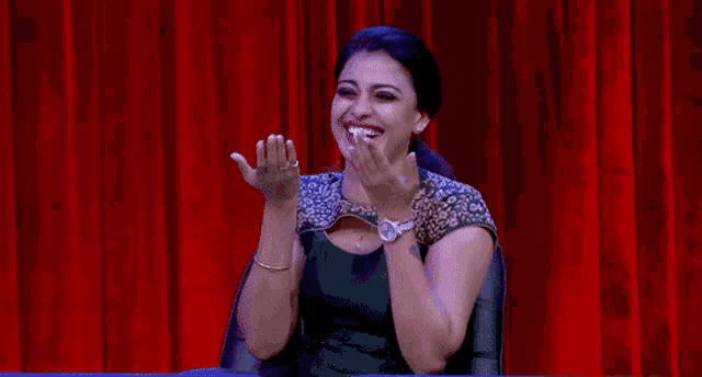 a woman covering her face with her hands in front of a red curtain
