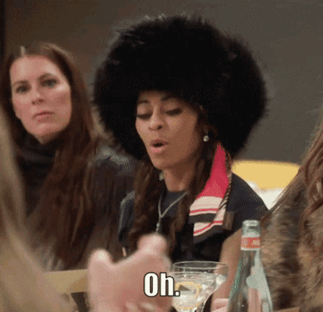 a woman wearing a fur hat says oh while sitting at a table with other women