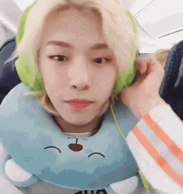 a young man wearing headphones and a blue neck pillow is sitting on an airplane .